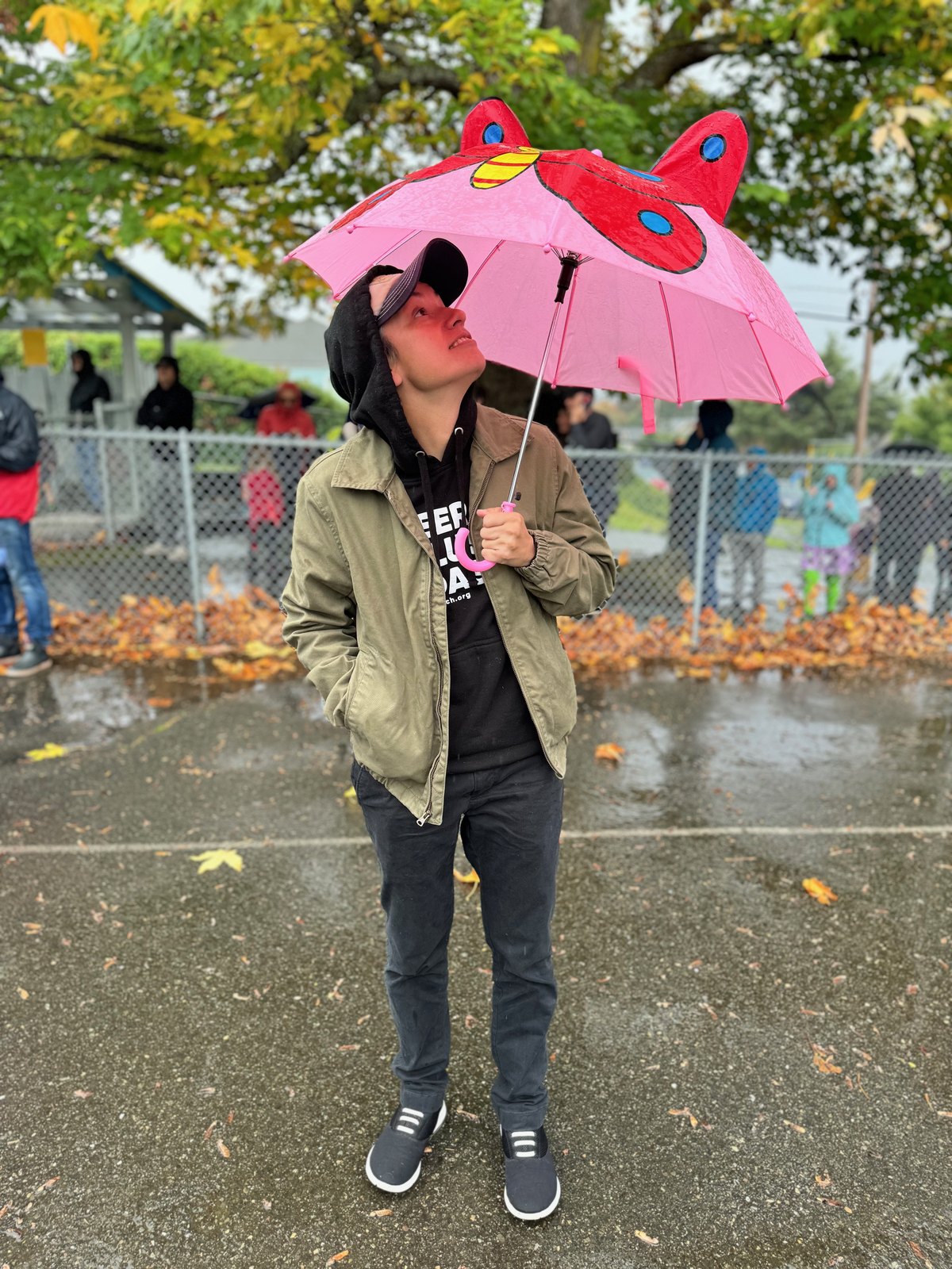 Riley looking up under a red and pink butterfly umbrella in the rain